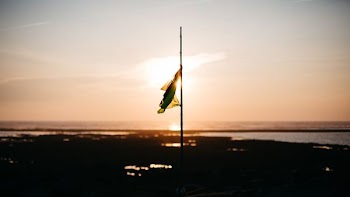 flag half mast near body of water during golden hour