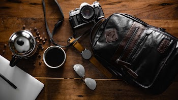 Flat Inlay Photography of Black Leather Backpack, Camera, Watch and Cup of Coffee
