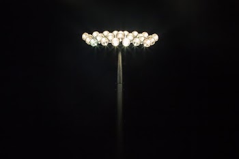 Floodlights shining at the top of a light pole with a pitch black background