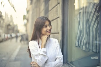 Focus Photo of Woman in White Long-sleeved Dress Standing at the Front of Gray Building