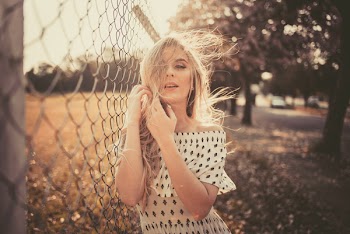 Focus Photography of Woman Leaning on Chain-link Fence While Holding Her Hair