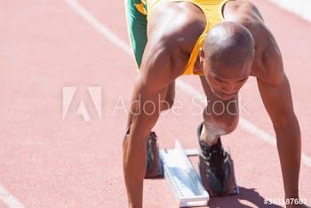 Focused male sprinter athlete ready at starting block on running track