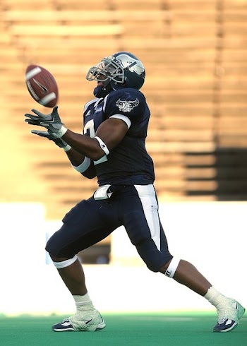 Football Player Wearing a Blue Jersey Catching a Football during Day Time