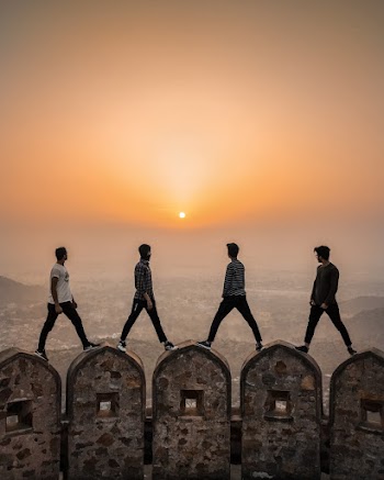 Four Men Standing on Arched Stone Walls With The View Of The Setting Sun Over A City