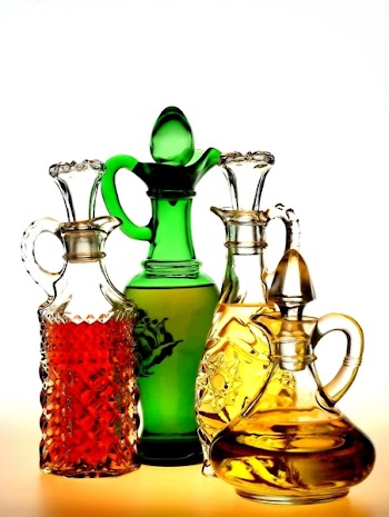 Four oil and vinegar salad dressing pitchers on a white background.