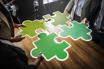 Four People Holding Four Jigsaw Pieces on Top of Brown Wooden Table