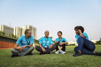 Four People Sitting On Grass Field 