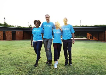 Four People Wearing Blue Crew-neck Shirts Standing on Lawn