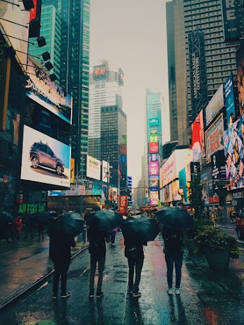 Four Person Under Umbrella Standing Near Buildings