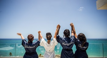 Four Women Holding Hands While Facing Body of Water