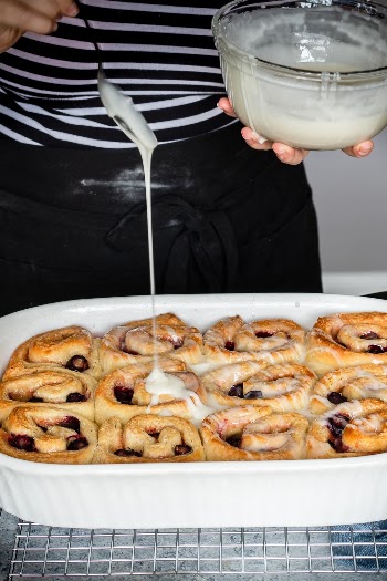 Frosting freshly baked sweet rolls with blueberries and strawberry jam.