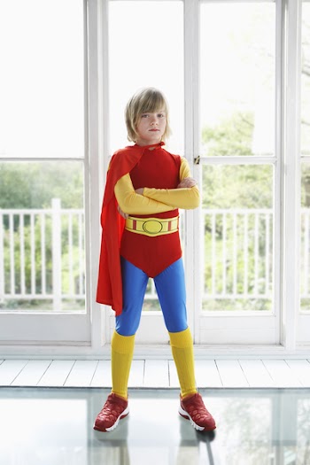Full length portrait of a serious young boy in superhero costume indoors