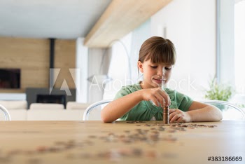 Girl counting and stacking coins at dining table