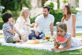 Girl eating watermelon on picnic blanket with family