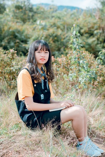 Girl in Black Dungaree and Orange Shirt Sitting of Grass Field