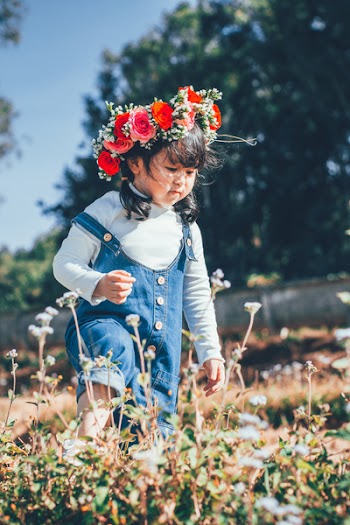 Girl In Blue Denim Dungaree With Red Flowers On Head Walking On Flower Field