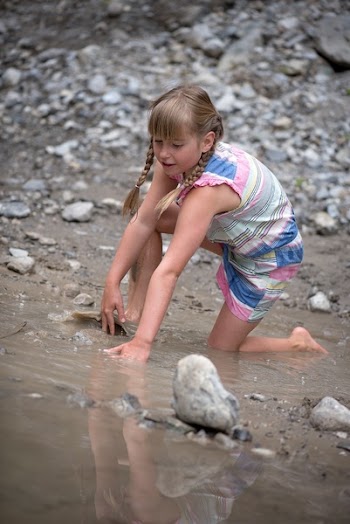 Girl in Pink White and Blue Romper in Body of Water With Gray Rocks