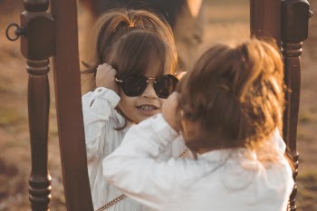 Girl in White Long-sleeved Shirt Wearing Sunglasses Facing Mirror