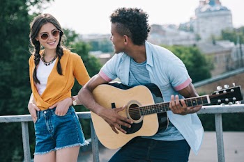 Girl listening to african american male guitarist performing on sunny city street