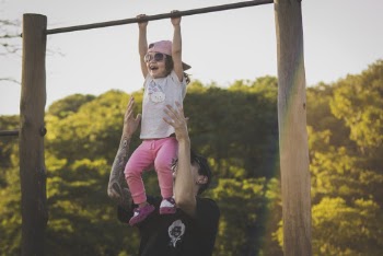 Girl on Monkey Bar With Father Assisting