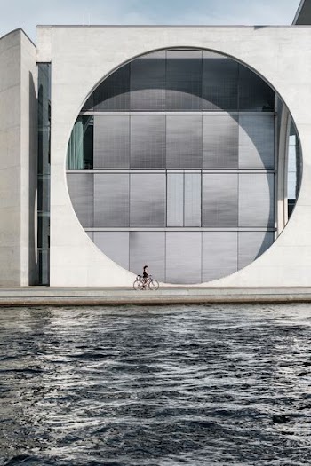 girl riding bike passing through body of water and building