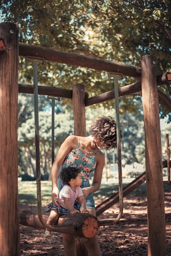 Girl Riding on Tree Log Swing Beside Woman Wearing Floral Dress