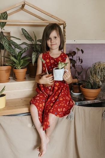 Girl Sits on Shelf Holding Planter