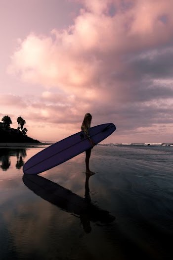 girl standing on shoreline carrying surfboard