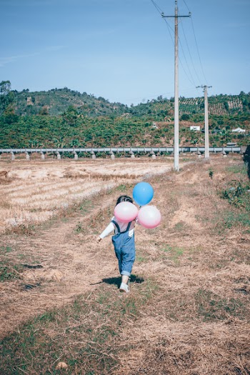 Girl Walking Holding Pink And Blue Latex Balloons 