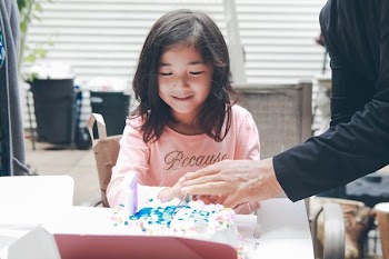 girl wearing pink crew-neck sweatshirt opening white-icing covered cake