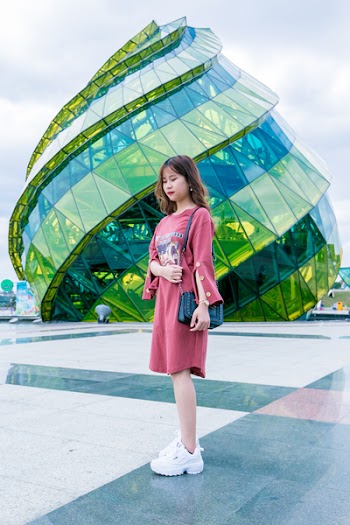 Girl Wearing Red Long-sleeved Dress and White Low-top Shoes Standing Near Green Glass Structure