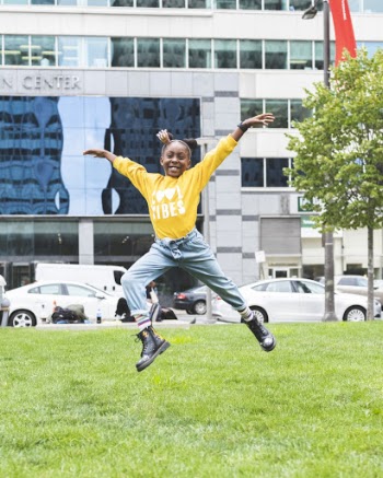 Girl Wearing Yellow Sweater Hopping on Green Grass