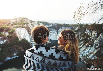Girlfriends cuddle together under blanket on top of the mountain