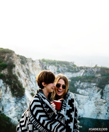 Girlfriends cuddle together under blanket on top of the mountain