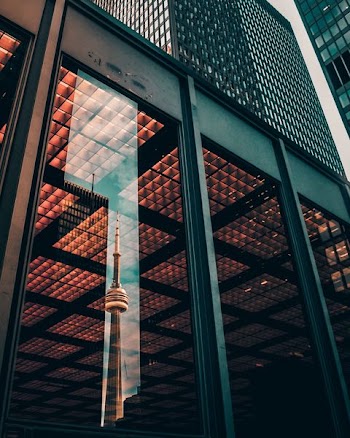 glass panel wall of building displaying the reflection of CNN Tower