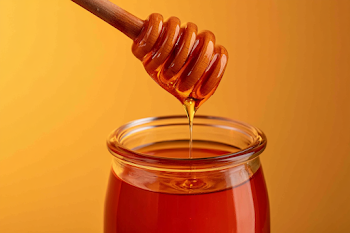 Golden Honey Dripping from Wooden Dipper into Jar