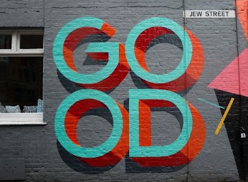 Graffiti art sign on a gray brick wall on Jew Street that reads "GOOD."