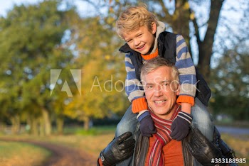 Grandfather carrying grandson on shoulders in autumn park