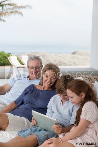 Grandparents and grandchildren using digital tablet on patio