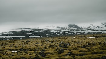 Grass Field On The Foot Of Hills And Mountains Covered With Snow at Distance