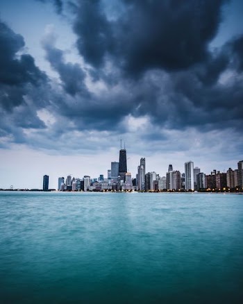 gray and black high-rise buildings beside body of water under gray and white sky at daytime