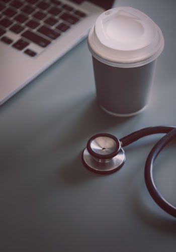 Gray and Black Stethoscope Beside Disposable Cup and Macbook Pro