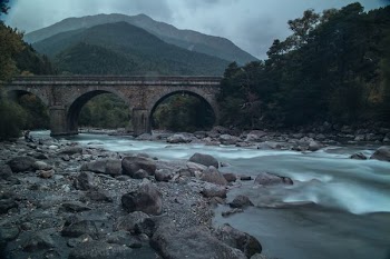 gray arch bridge over river under gray sky at daytime