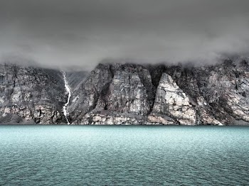 gray cliff beside body of water covered by fog