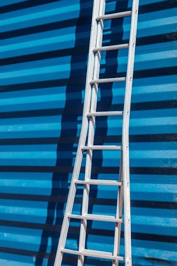 gray metal ladder leaning on blue corrugated sheet