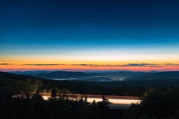 gray road surrounded by trees overseeing mountain rage during nighttie