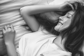 Gray scale close-up photography of a woman in crew-neck top lying down while touching her head with her eyes closed 