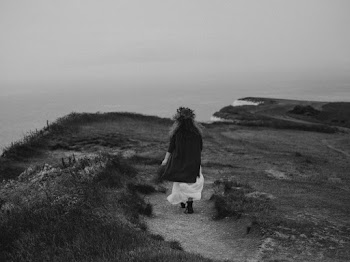 Gray Scale Photo of Woman Walking across Dry Grass Field