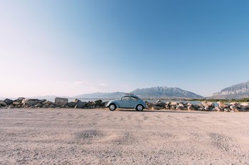 gray Volkswagen Beetle on dirt road near body of water and mountains at daytime