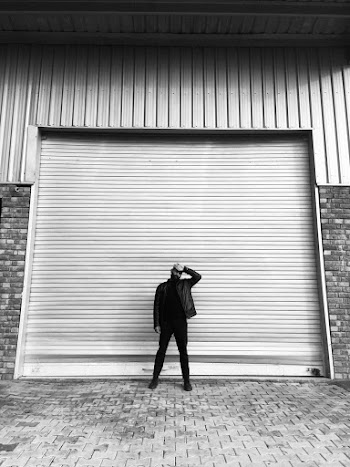 Grayscae Photo of Man Standing in Front of Closed Roll-up Door